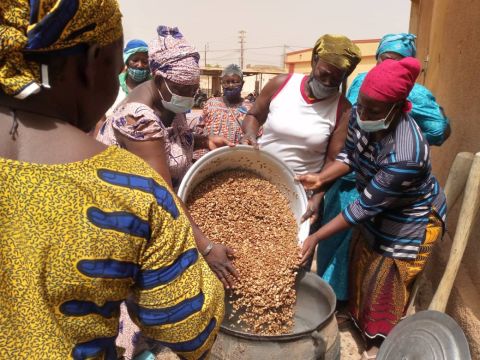 Burkinabe women pouring a giant pot of African locust bean seeds into boiling water for soumbala spice preparation; Credit: Jocelyne Vokouma (2024)