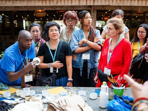 Idrissa explaining to the participants the various stations for the workshop, from the soaking of the cloth to prepare it for designing, the drying process, and the samples prepared to create patterns.